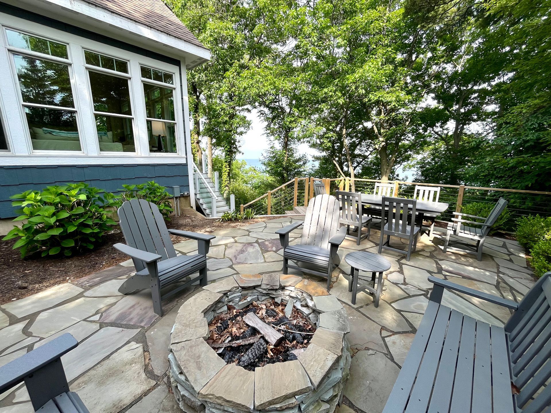 A fire pit on a patio with chairs and tables in front of a house.