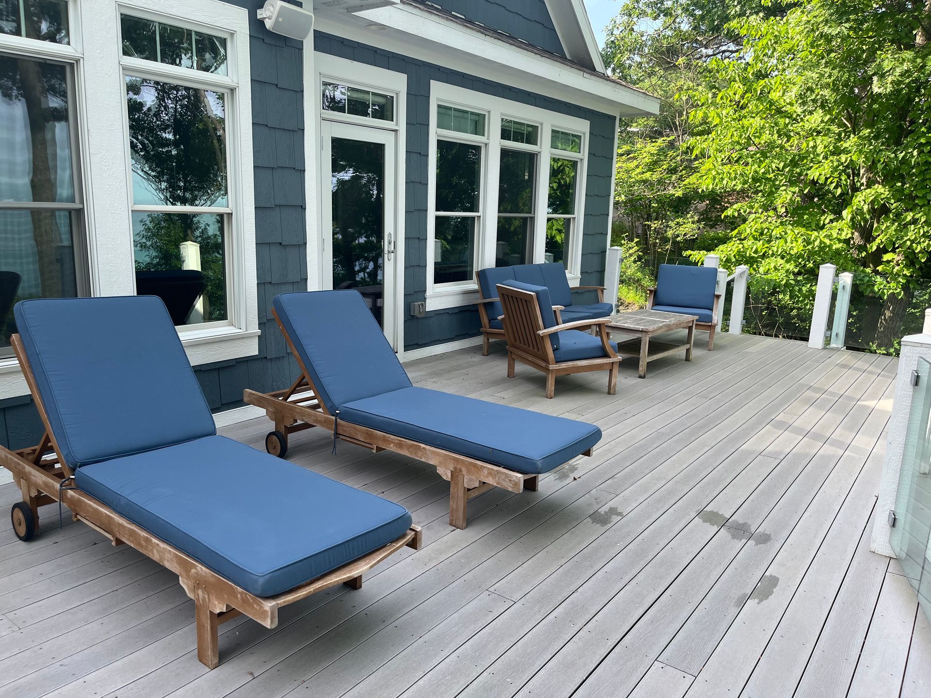 A deck with blue lounge chairs and a table in front of a house.