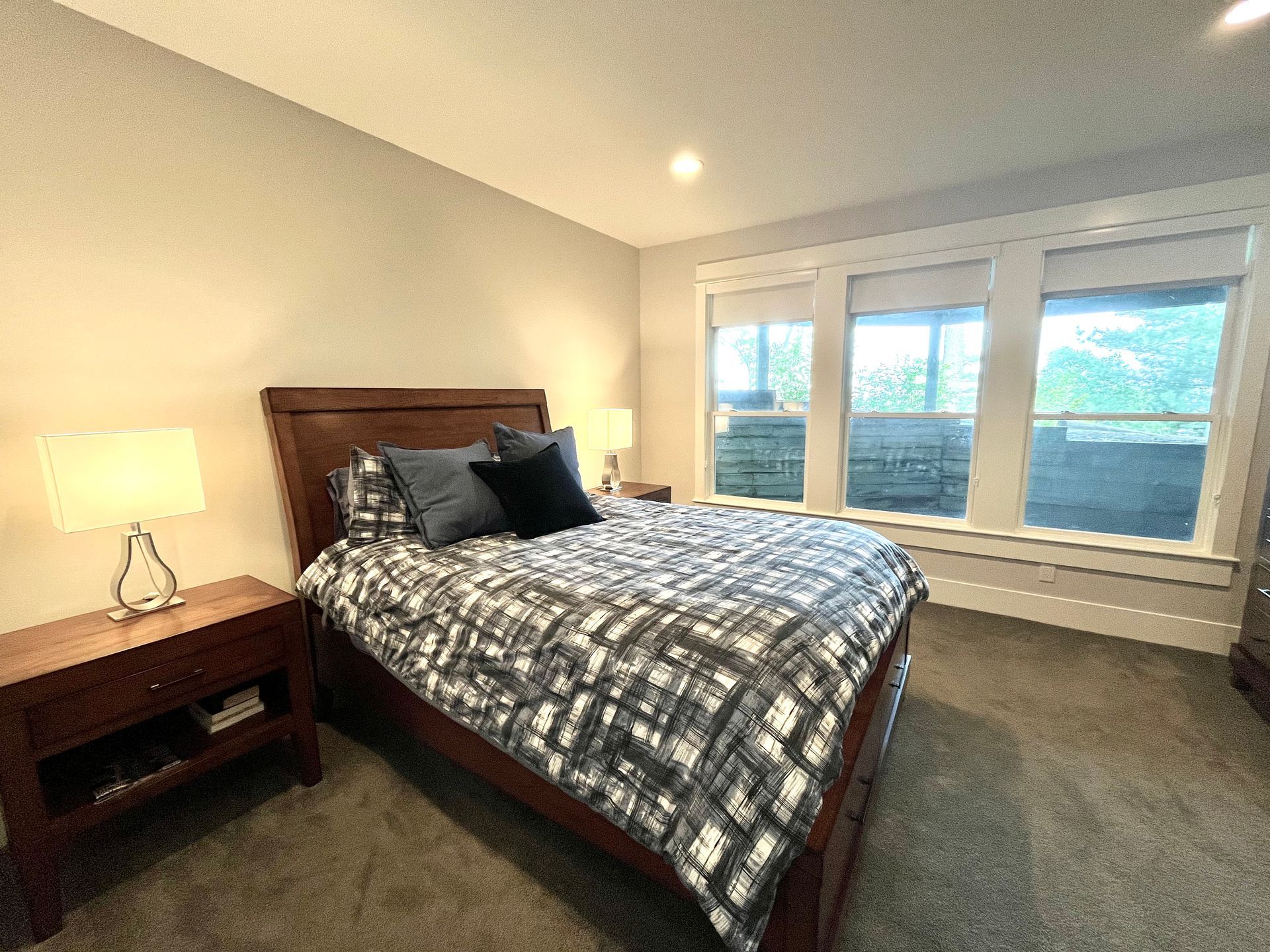 A bedroom with a bed , nightstand , and two windows.