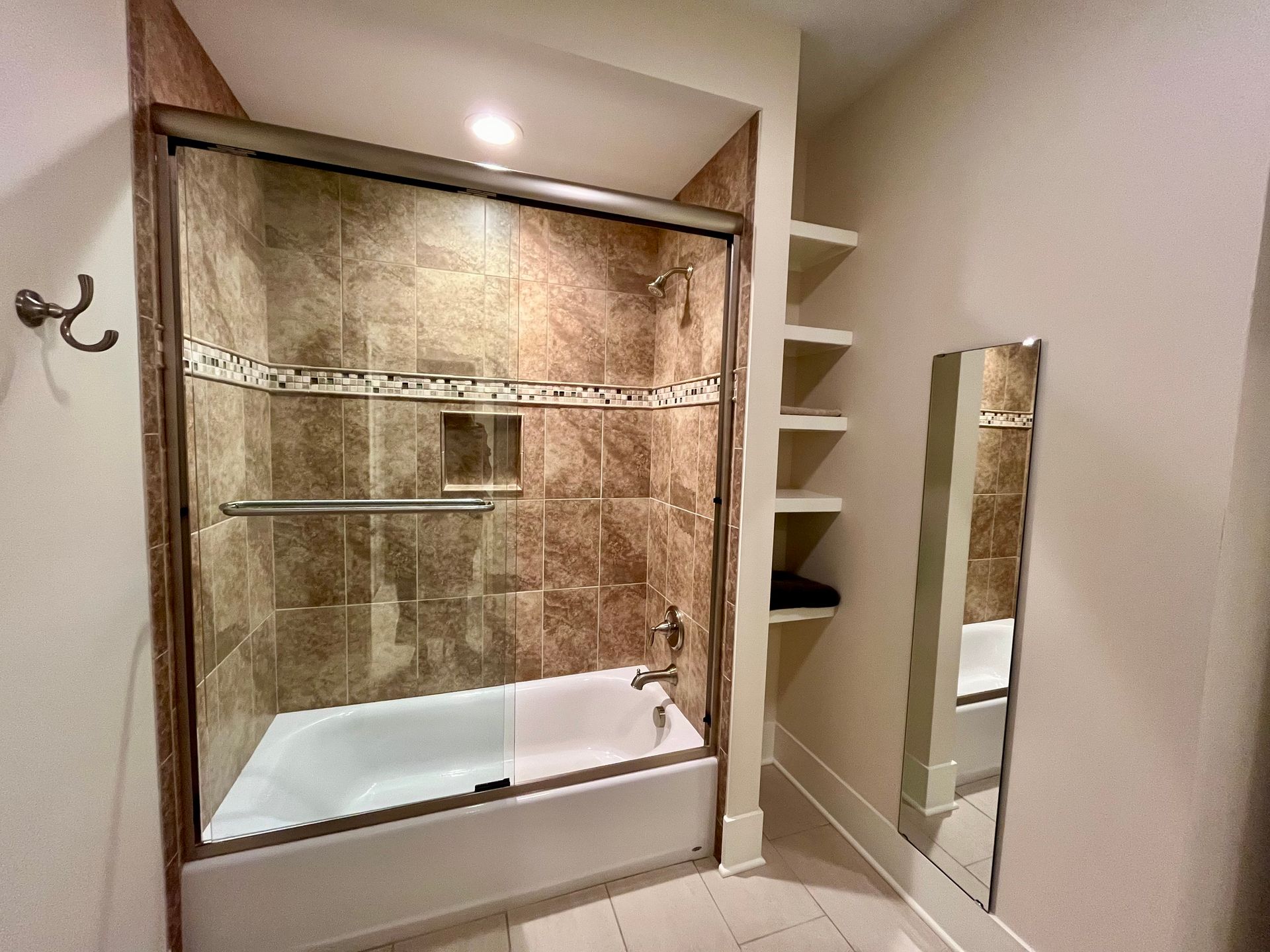 A bathroom with a bathtub , shower , mirror and shelves.