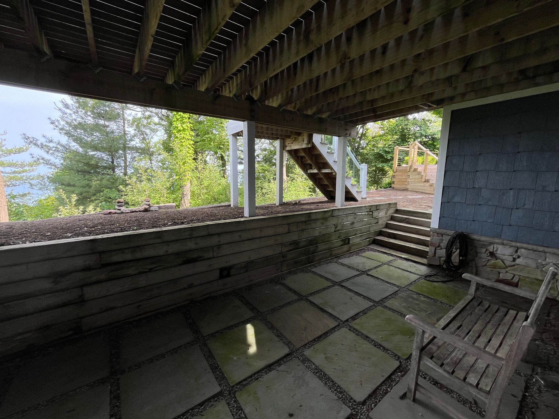 A patio with a bench and stairs under a wooden deck.