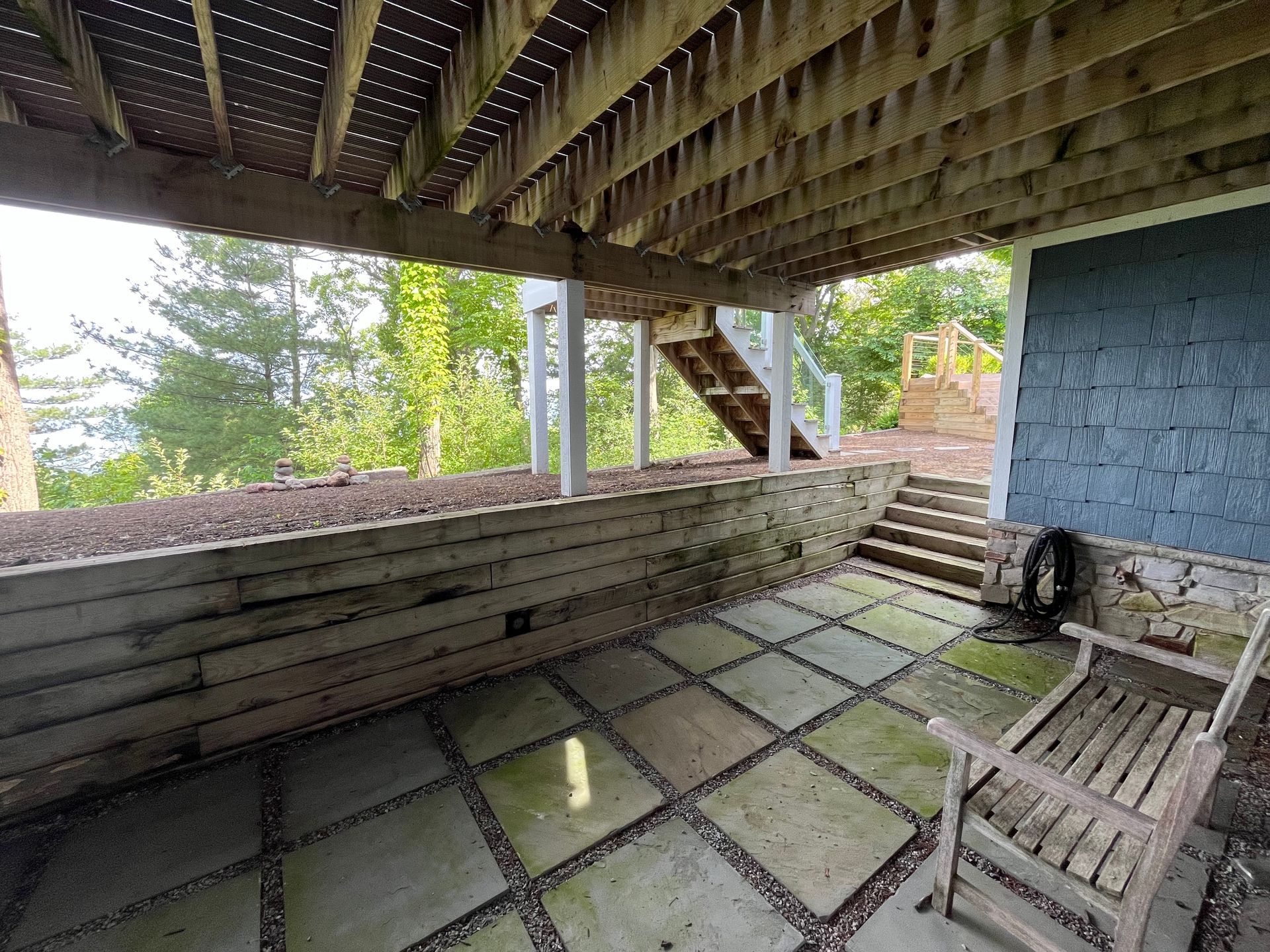 A patio with a bench and stairs under a wooden deck.