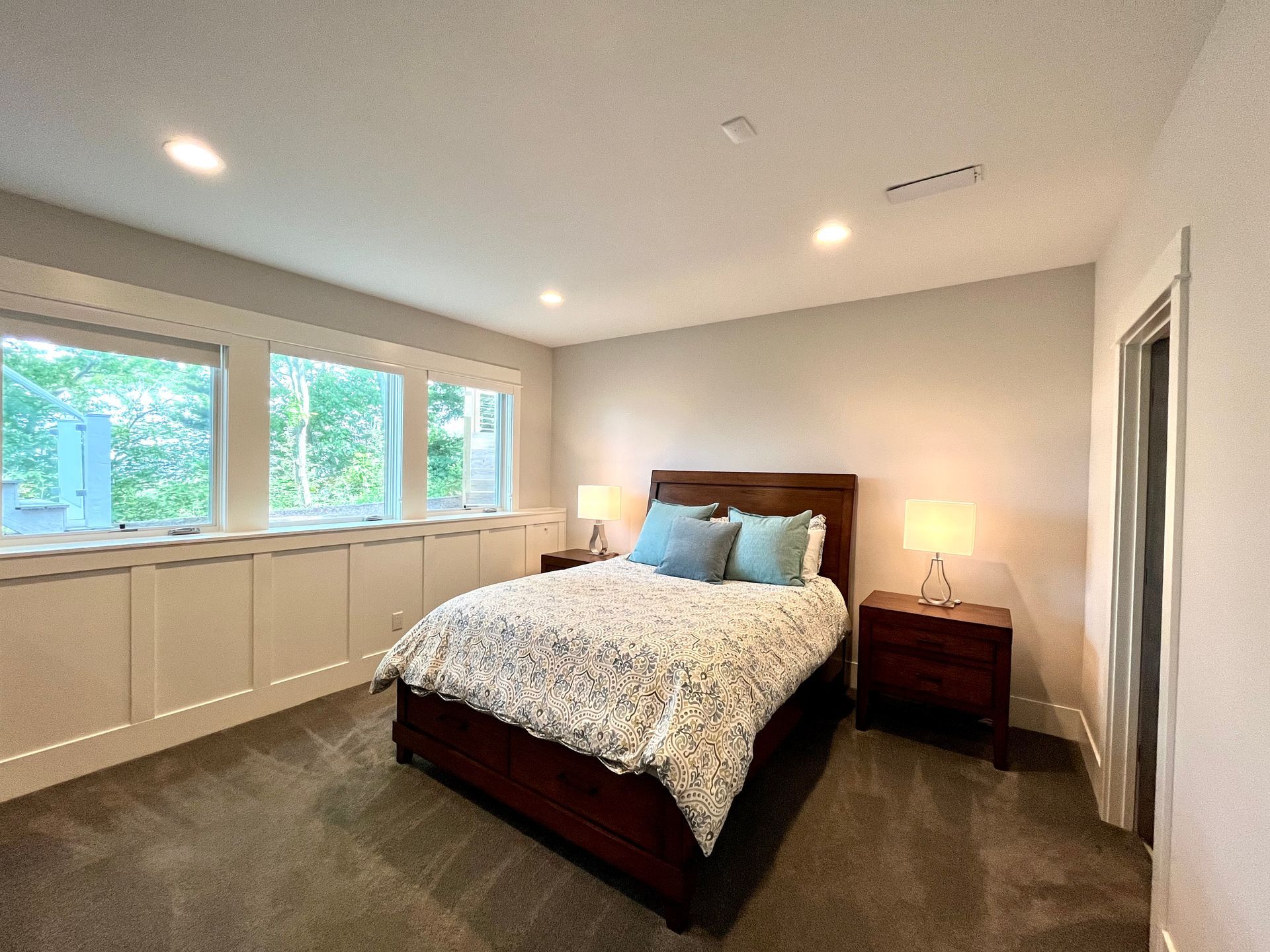 A bedroom with a bed , two nightstands , and a lot of windows.
