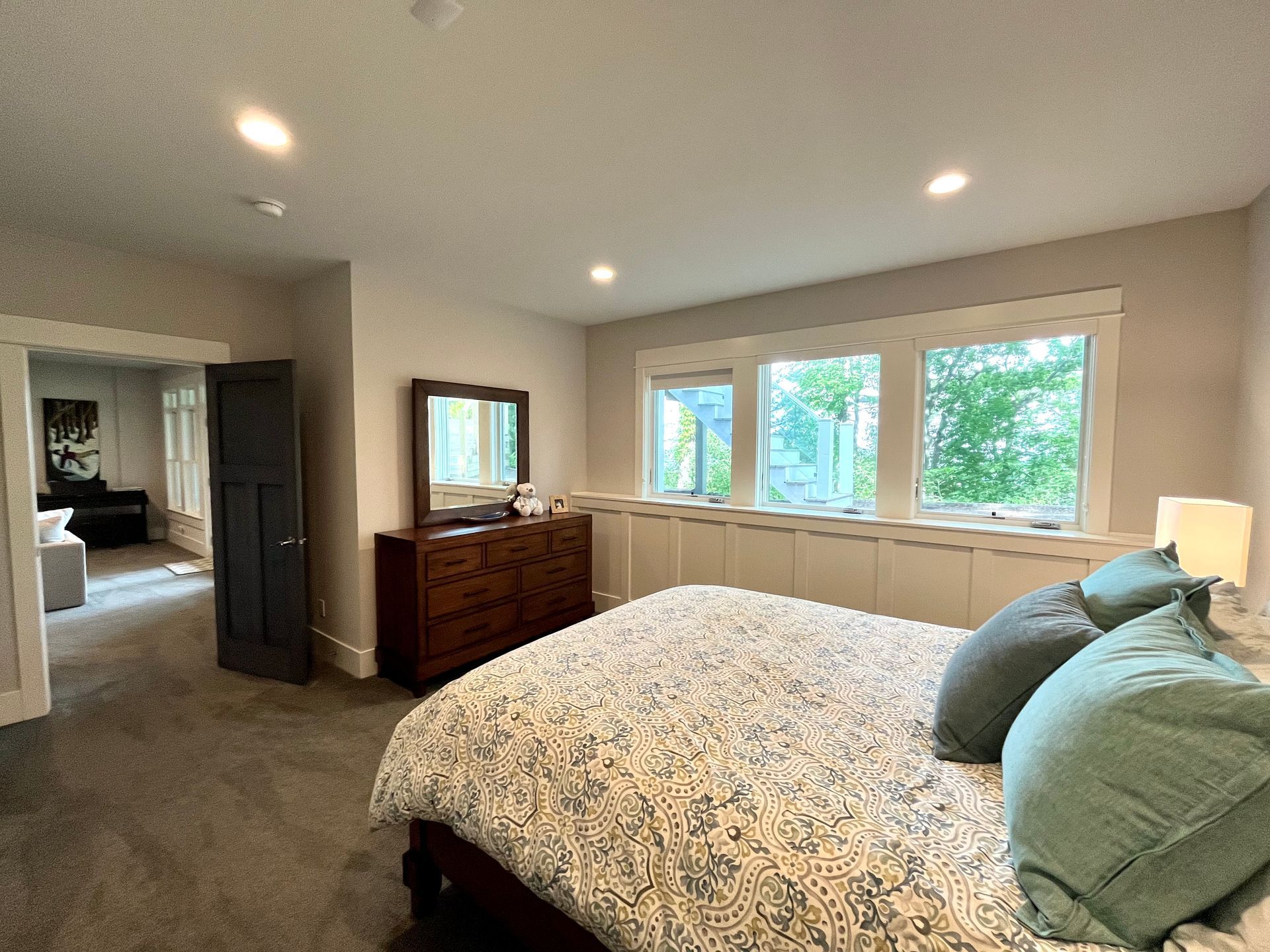 A bedroom with a king size bed , dresser , mirror and lots of windows.