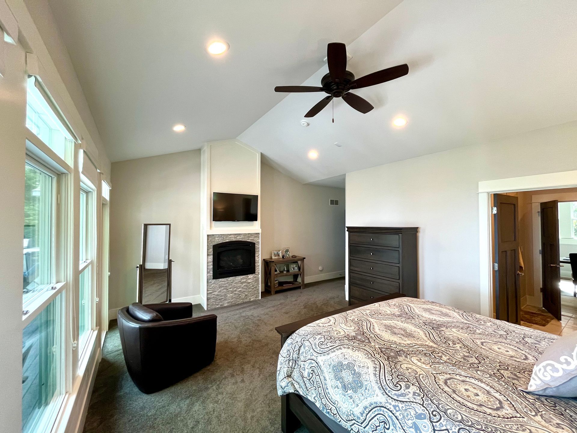A bedroom with a bed , chair , fireplace and ceiling fan.