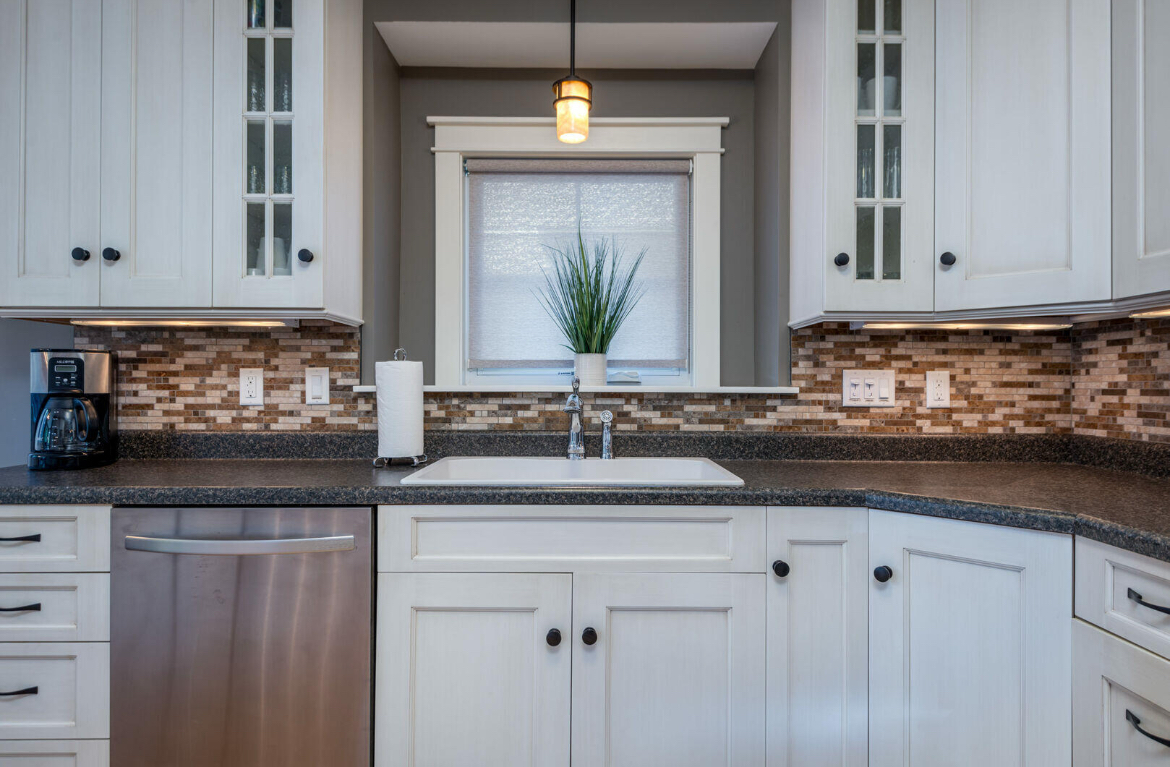 A kitchen with white cabinets , stainless steel appliances , a sink , and a window.