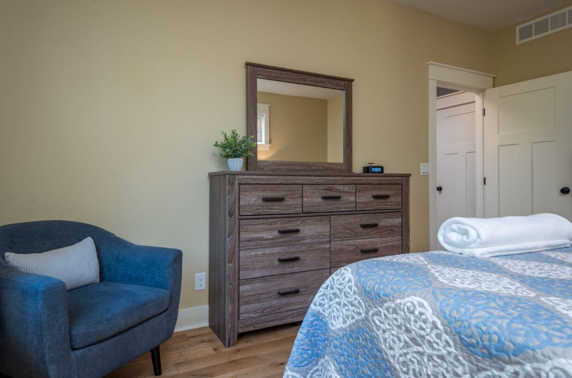 A bedroom with a bed , dresser , chair and mirror.
