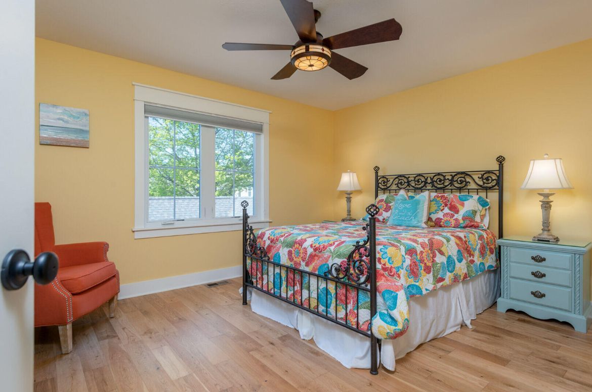 A bedroom with a bed , nightstand , chair and ceiling fan.