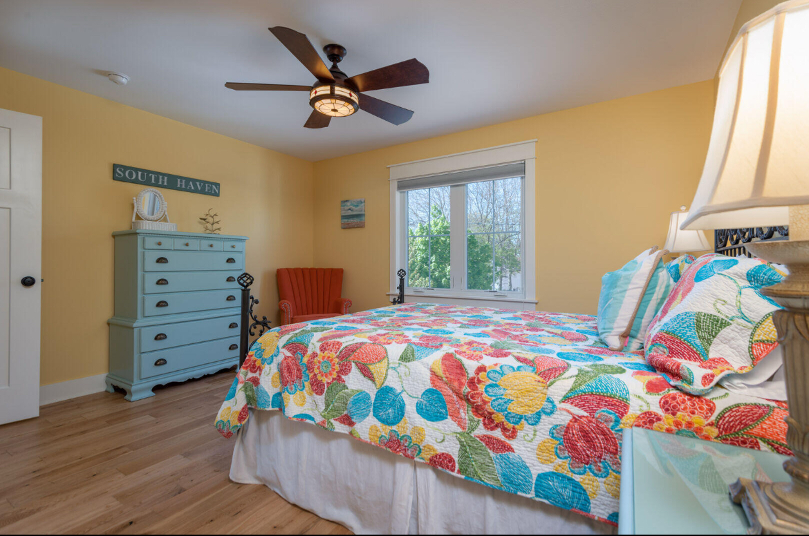 A bedroom with a bed , dresser , lamp and ceiling fan