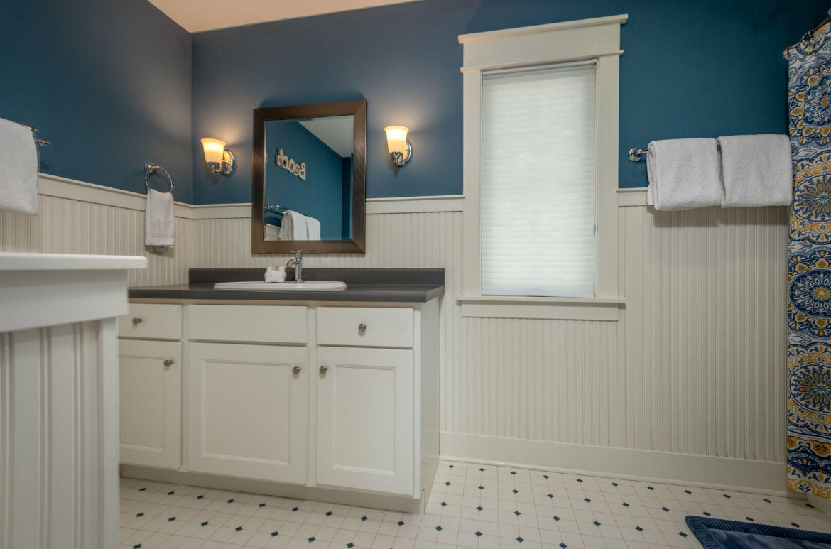 A bathroom with blue walls , white cabinets , a sink and a mirror.