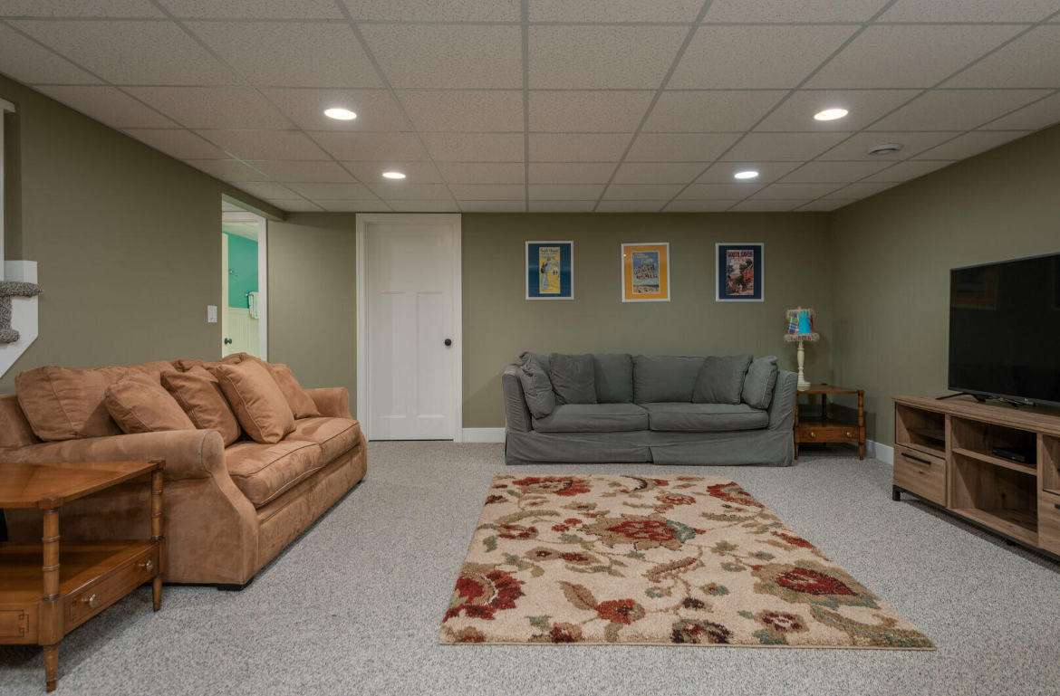 A living room in a basement with a couch , rug and television.