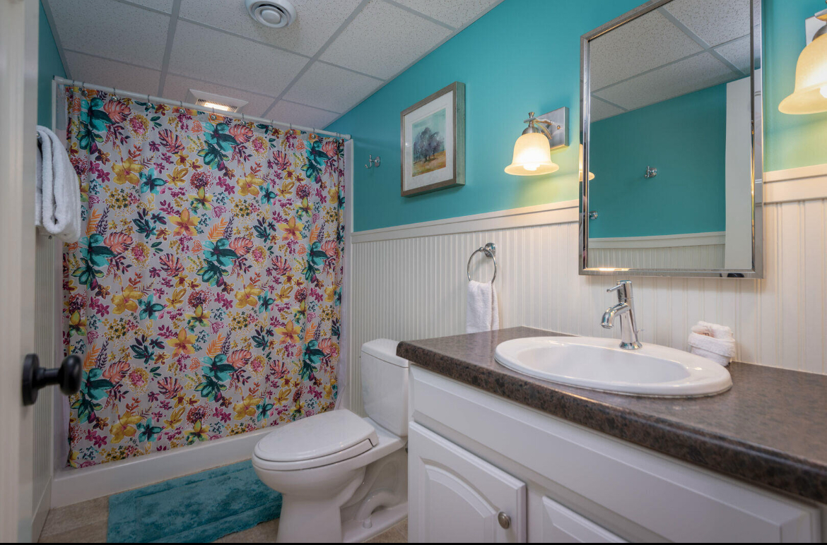 A bathroom with a toilet , sink , mirror and shower curtain.
