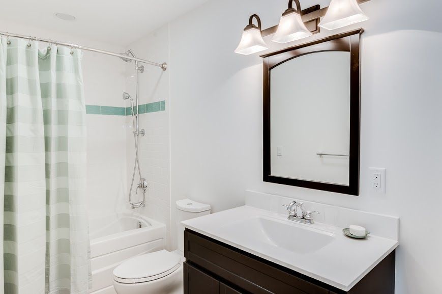 Bright bathroom with white shower curtain, toilet, vanity, and mirror under three-light fixture
