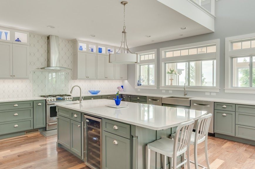 Bright kitchen with white cabinets, sage island, marble countertops, and large windows