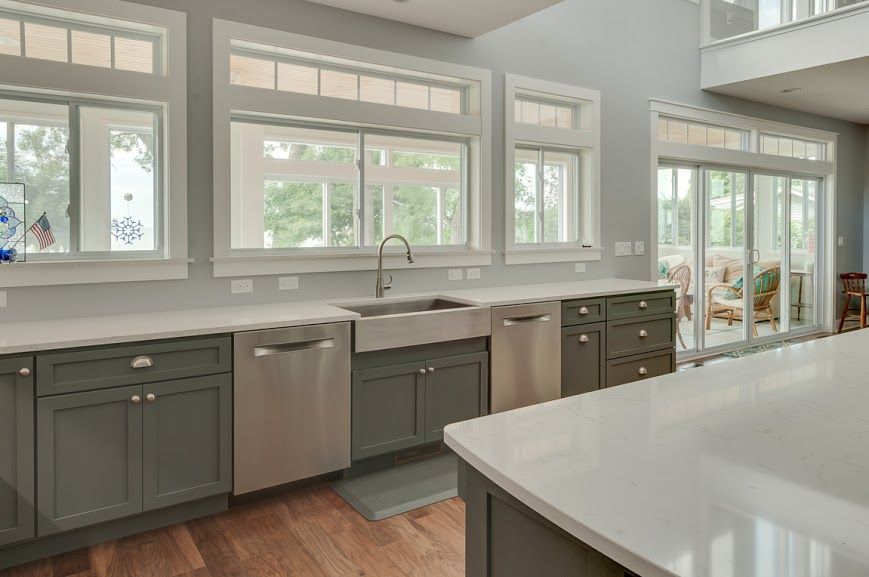 A kitchen with stainless steel appliances , gray cabinets , and white counter tops.