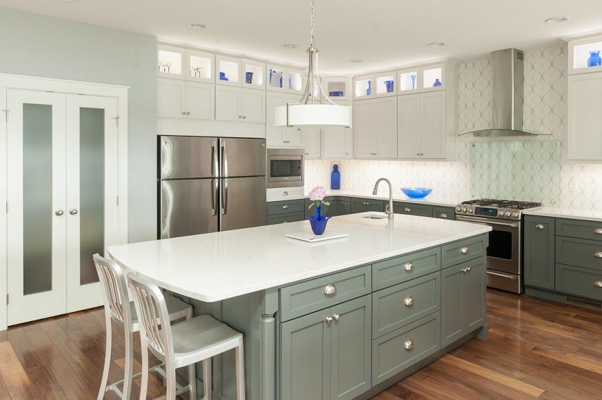 A kitchen with gray cabinets , white counter tops , stainless steel appliances and a large island.