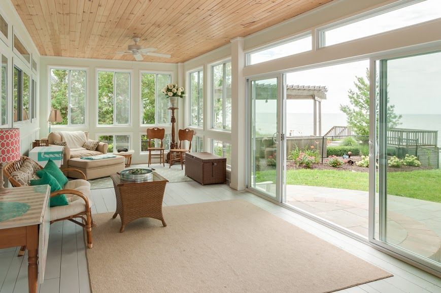 Bright sunroom with wicker seating, beige carpet, and large sliding glass doors opening to a patio and garden.