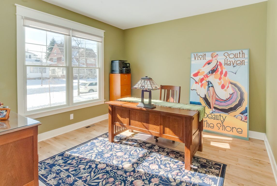 A home office with a desk , chairs , and a large painting on the wall.