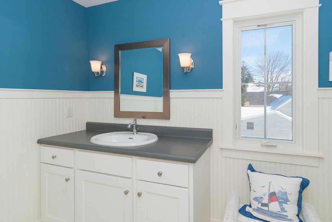 A bathroom with blue walls , a sink , a mirror and a window.