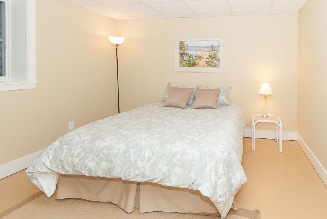 A bedroom with a bed , lamp , nightstand and picture on the wall.