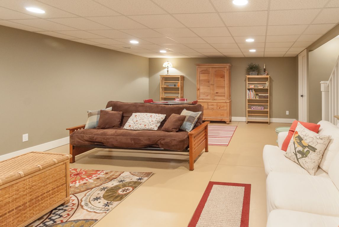 A living room in a basement with a couch , two couches , and a rug.