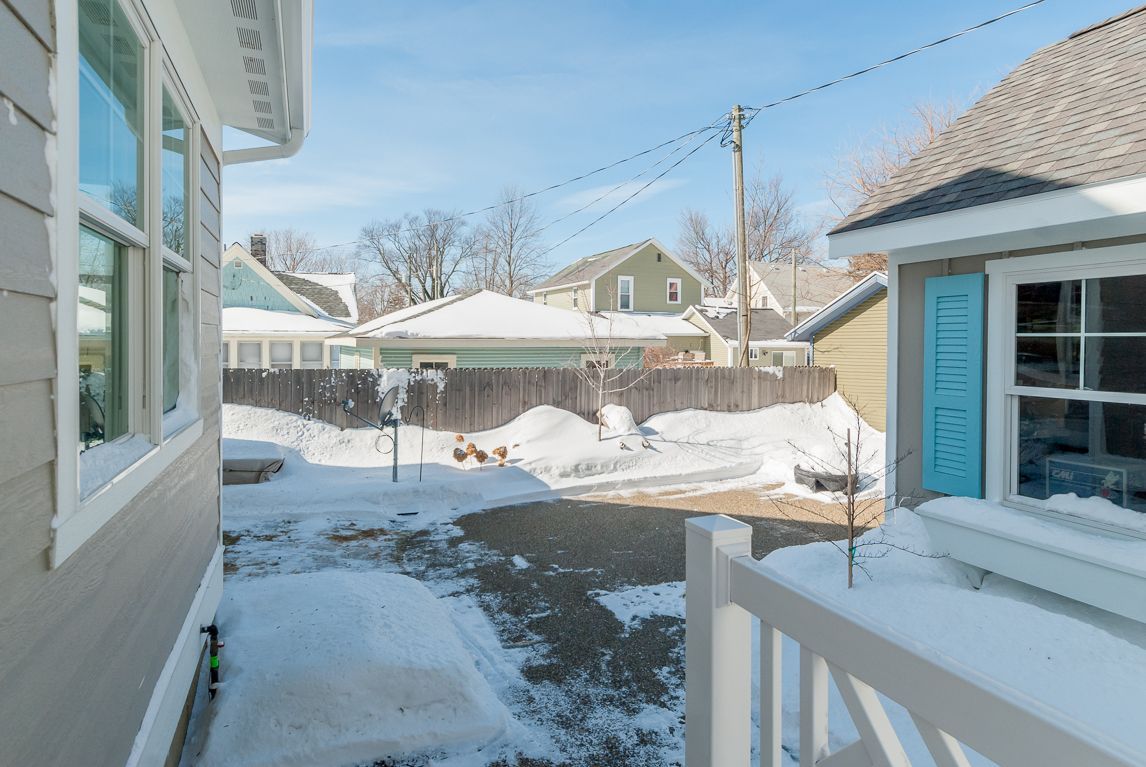 A snowy backyard with a white fence and a house in the background.