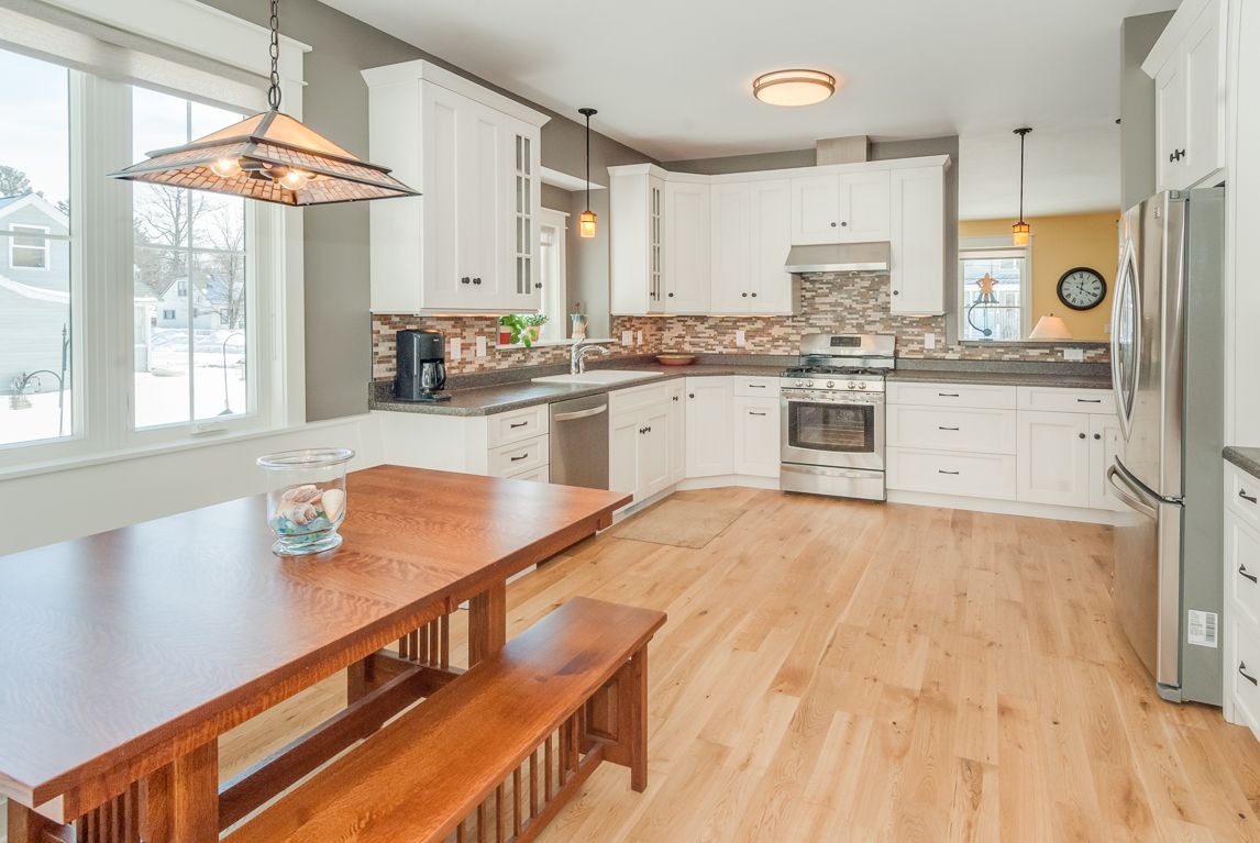 A kitchen with white cabinets , stainless steel appliances , hardwood floors and a wooden table and bench.