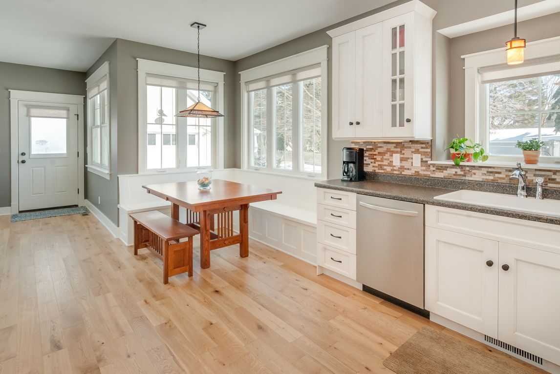 A kitchen with white cabinets , stainless steel appliances , a table and bench.