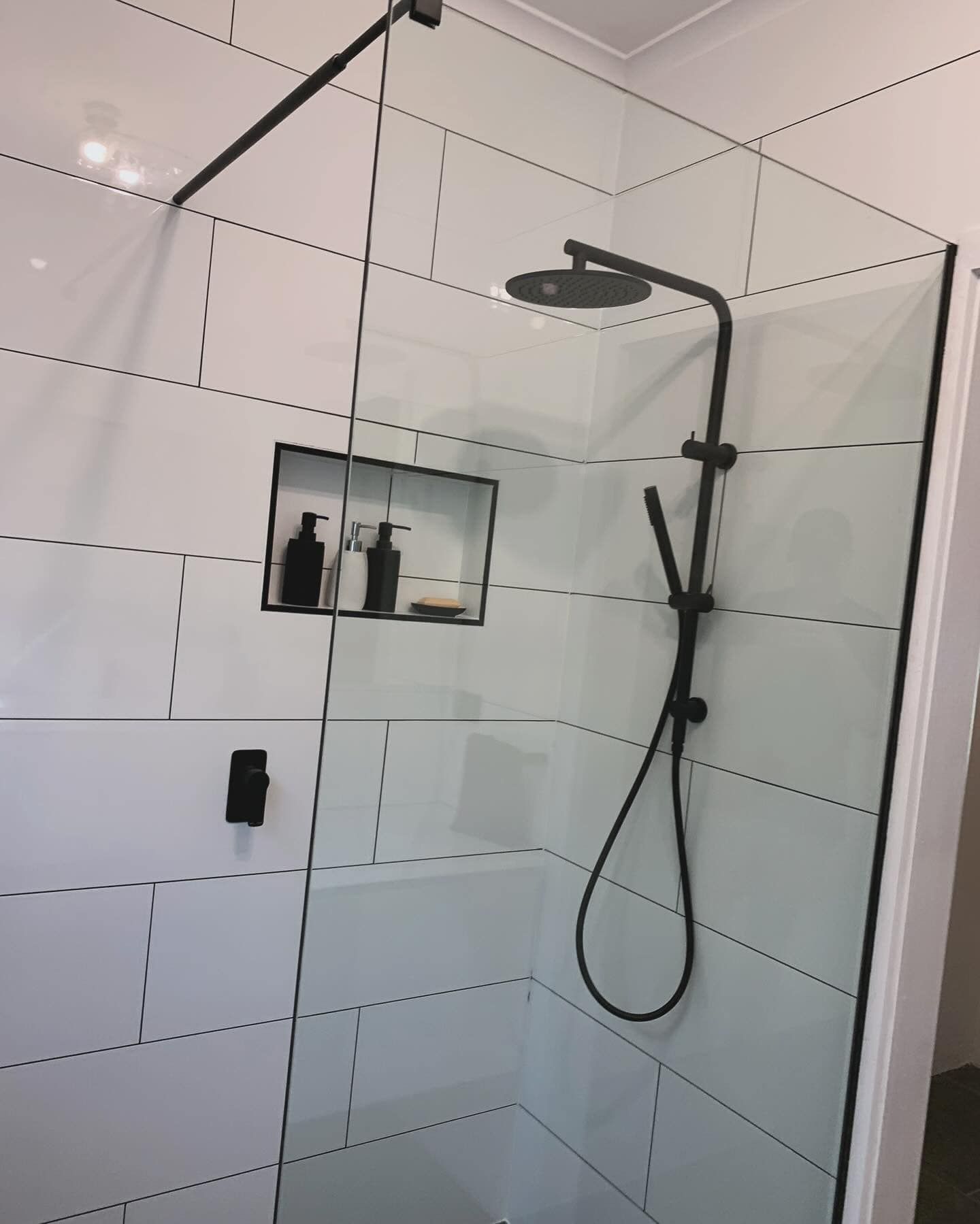 A modern bathroom shower with black fixtures, glass walls, and white tiled walls.