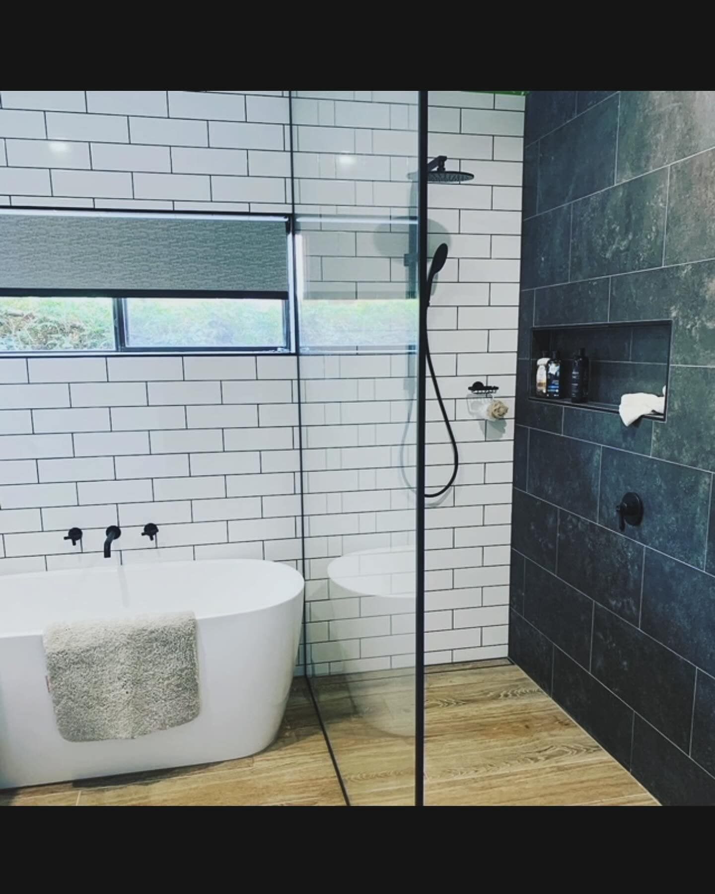 Modern bathroom with white tub, glass shower, and gray tile walls.