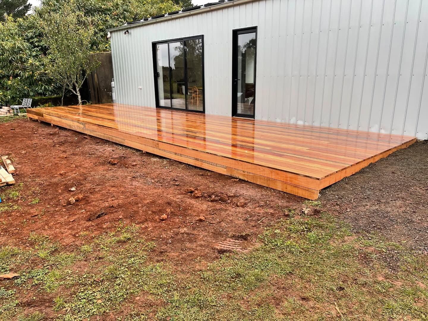 Wooden deck attached to a modern white building with large windows, set in a grassy yard.