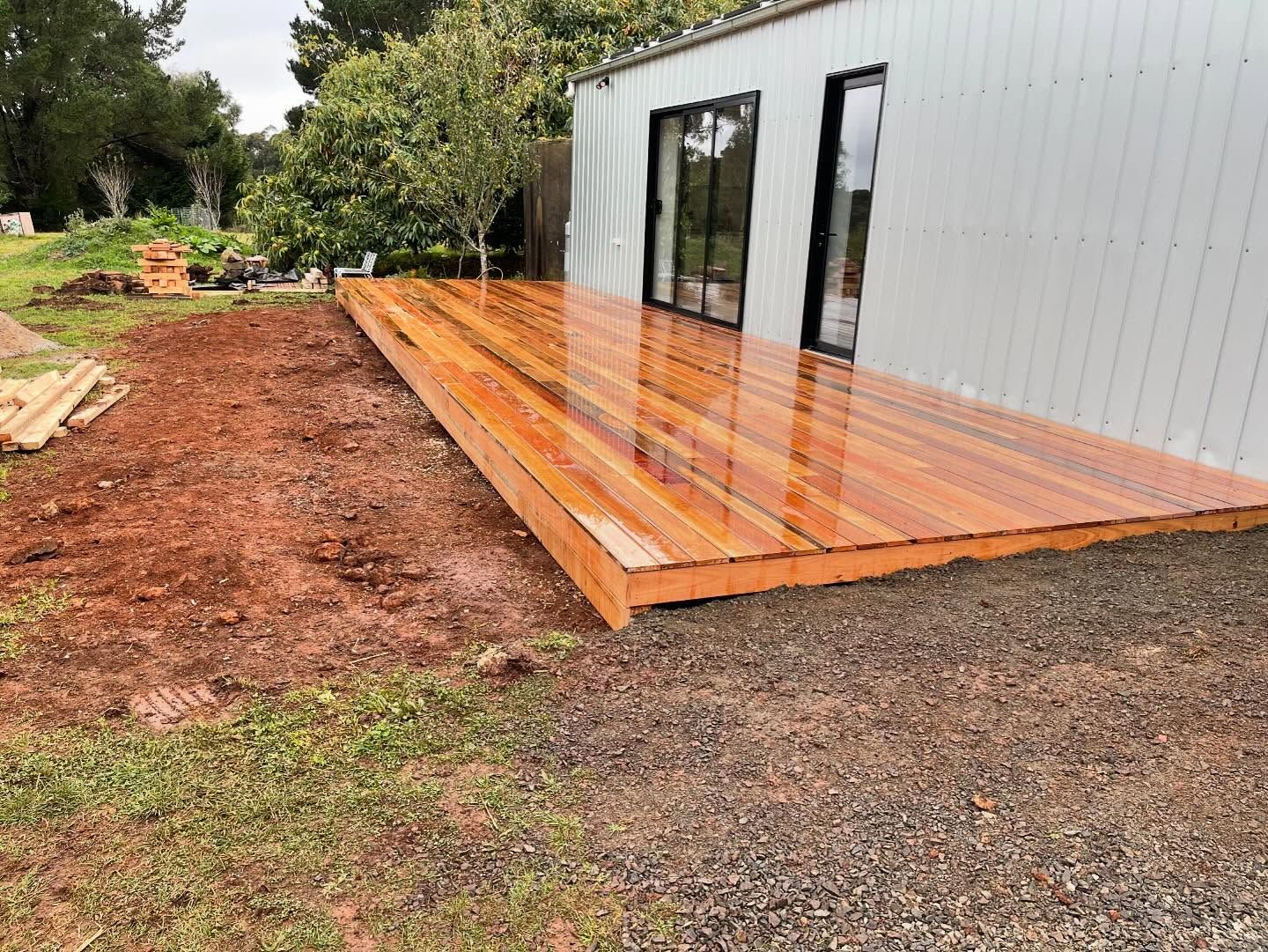 Wooden deck attached to a building, surrounded by dirt and gravel.
