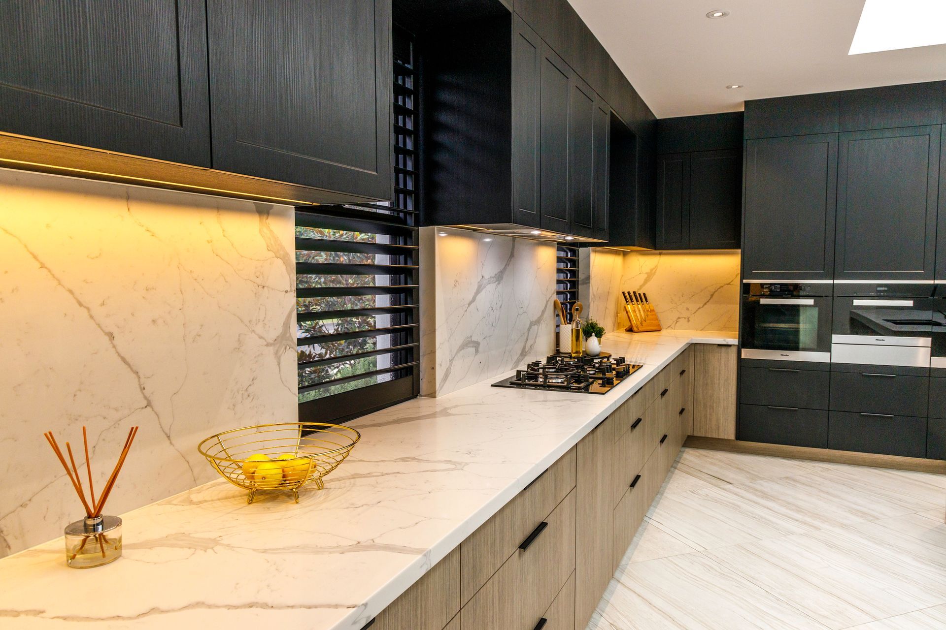 Modern kitchen with dark cabinets, marble backsplash and countertops, and recessed lighting.