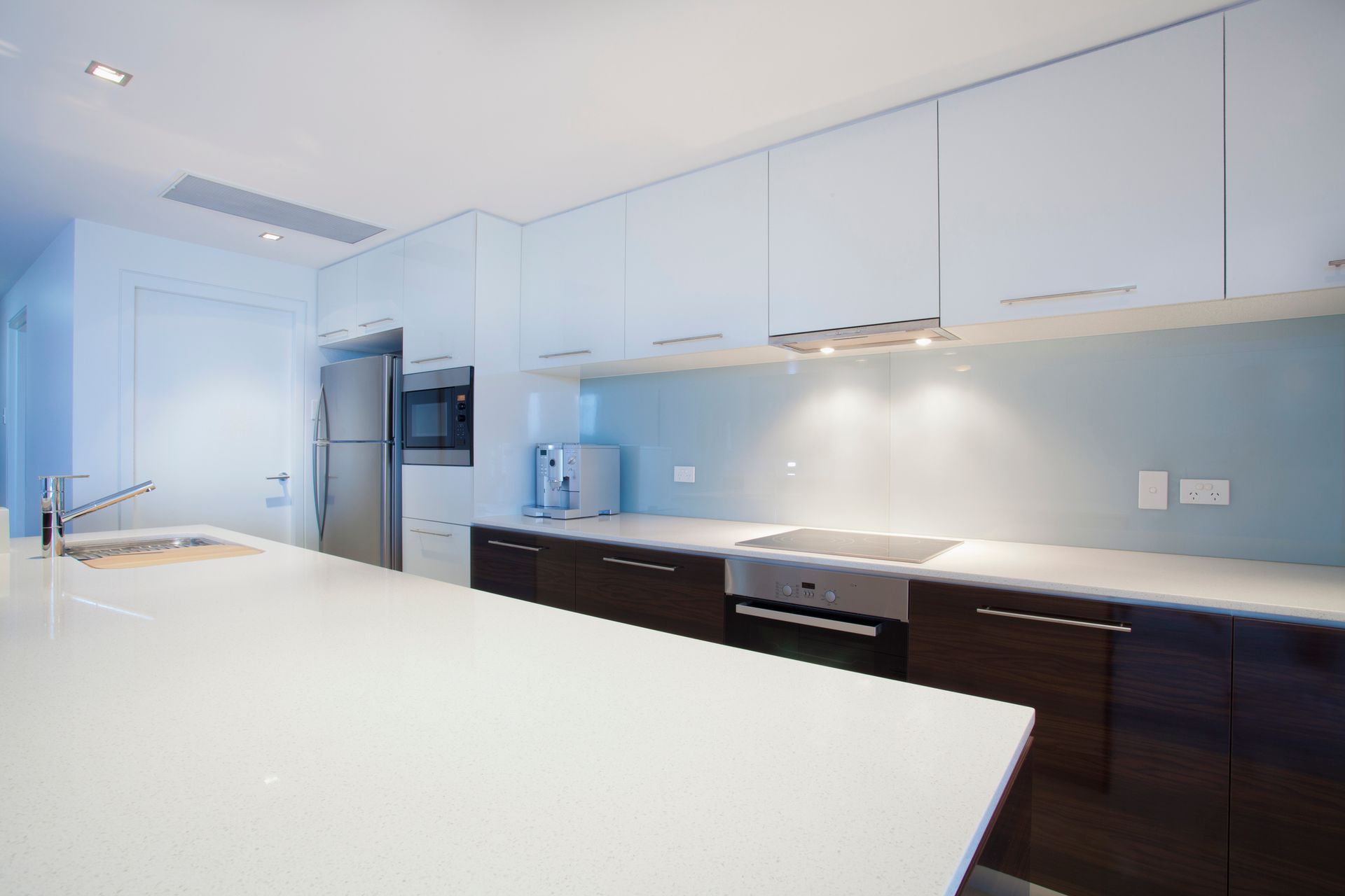 Modern kitchen with white countertops, dark cabinets, stainless steel appliances, and light blue backsplash.