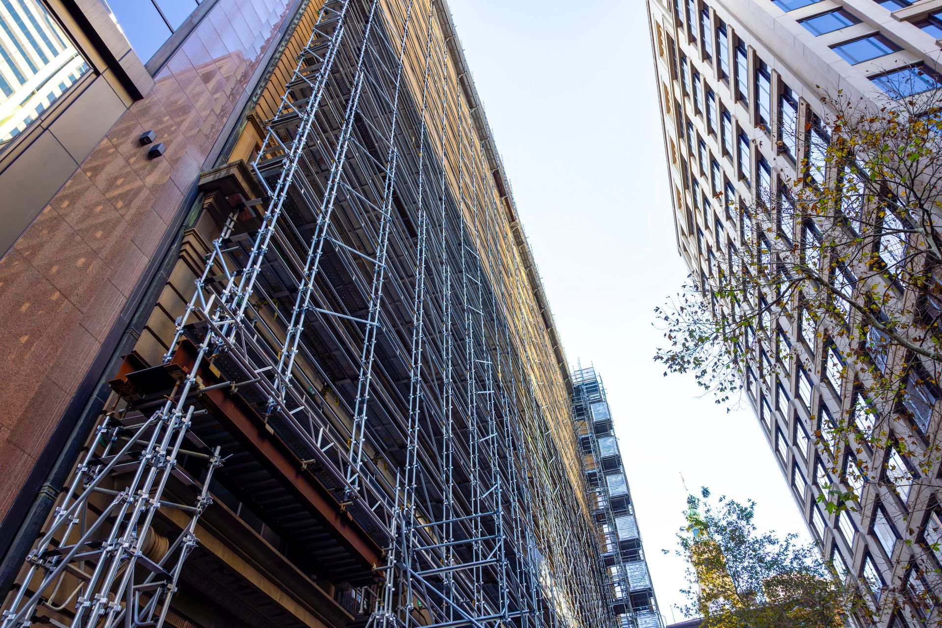 Building under construction with scaffolding, viewed from a low angle, flanked by other buildings.