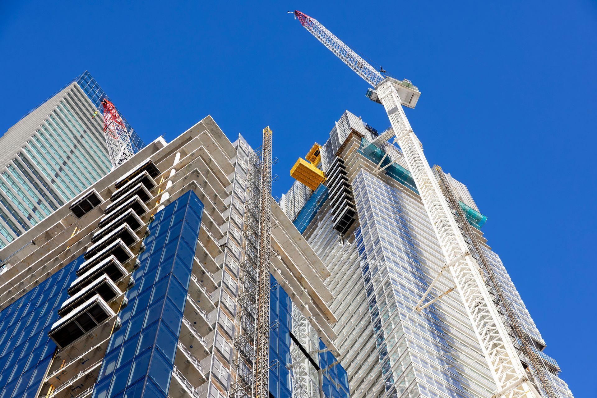 Construction site with tall buildings, cranes, and a clear blue sky.