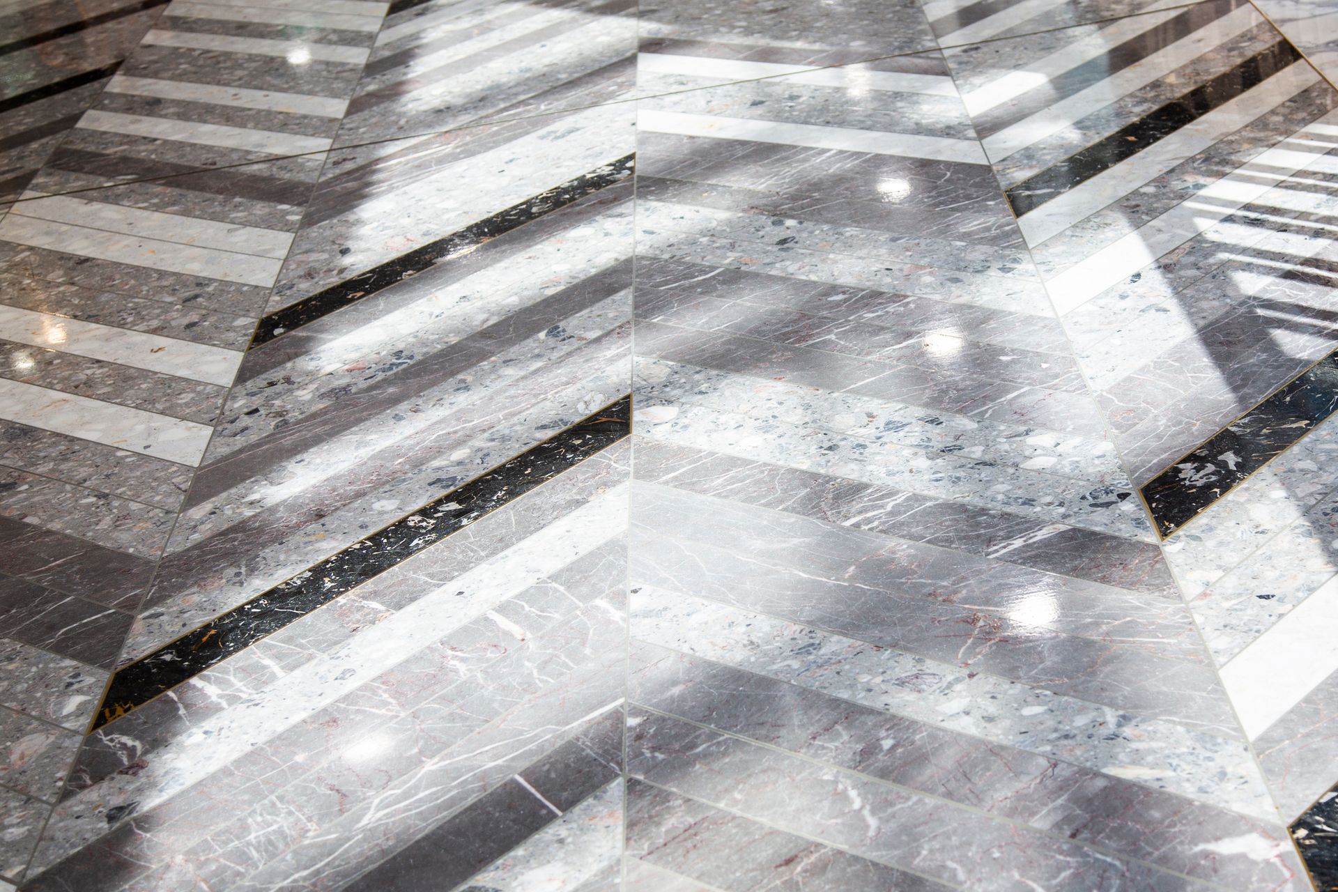 Gray and white marble floor with a chevron pattern reflecting light.