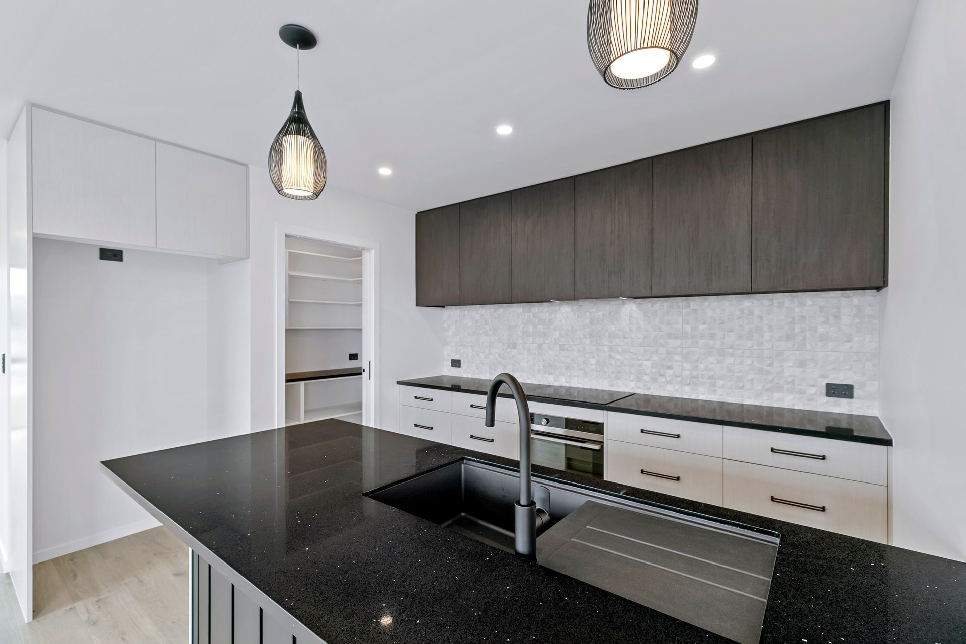 Modern kitchen with black countertops, dark upper cabinets, and white lower cabinets; pendant lights.