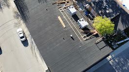 Aerial view of a flat, black rooftop with equipment and a car on the street.