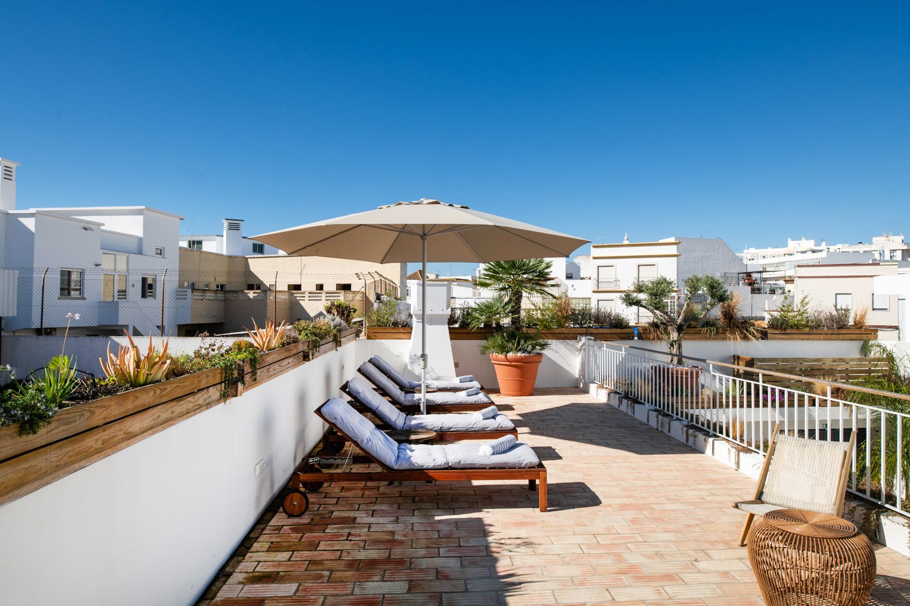 a rooftop terrace with a row of lounge chairs and an umbrella .
