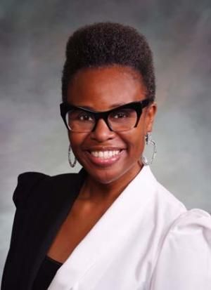 A woman wearing glasses and hoop earrings is smiling for the camera.