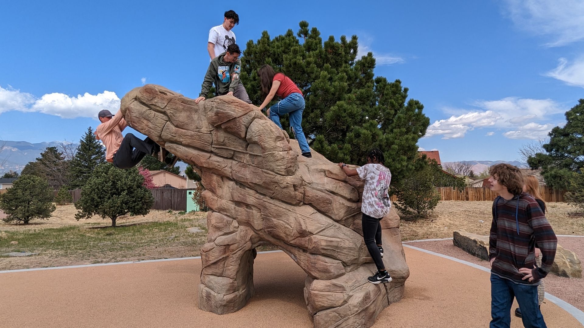 Youth climb a rock-like structure at a park