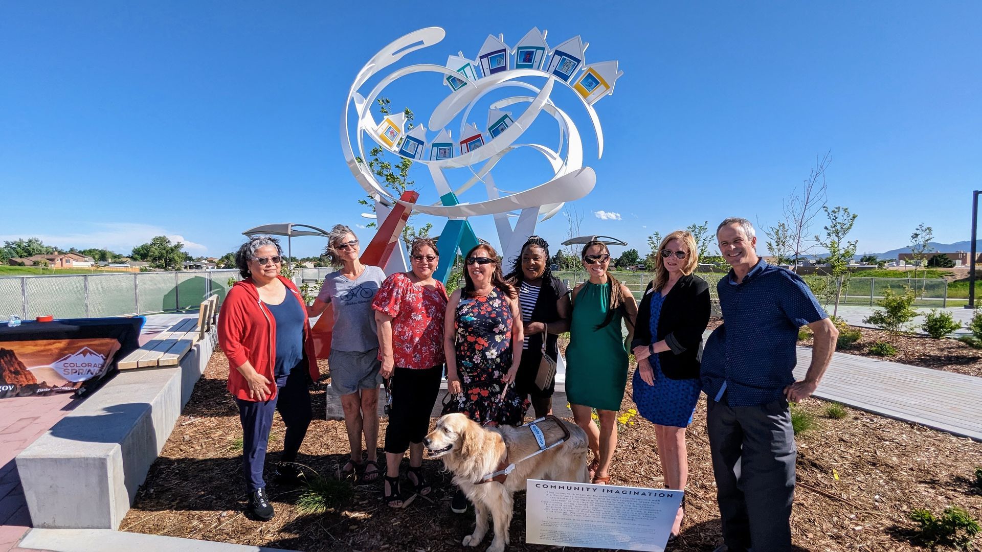 A group of eight adults and a guide dog in front of an art installation
