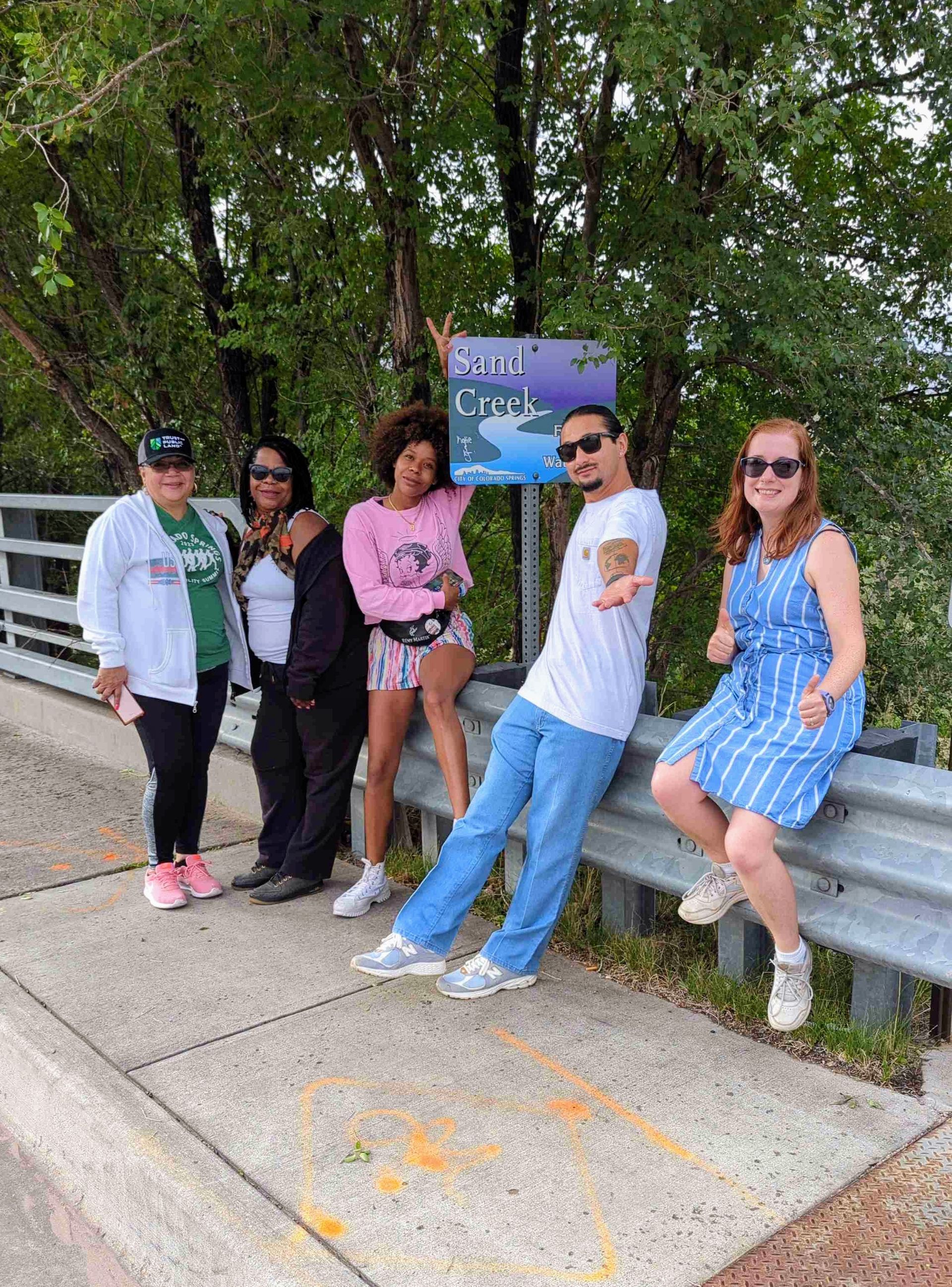 A group of five people on a city sidewalk in front of a sign for the sand creek