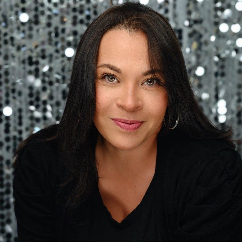 A woman with long dark hair is wearing a black shirt and smiling for the camera.