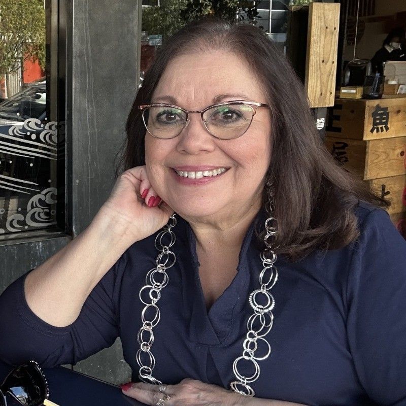 A woman wearing glasses and a necklace smiles for the camera