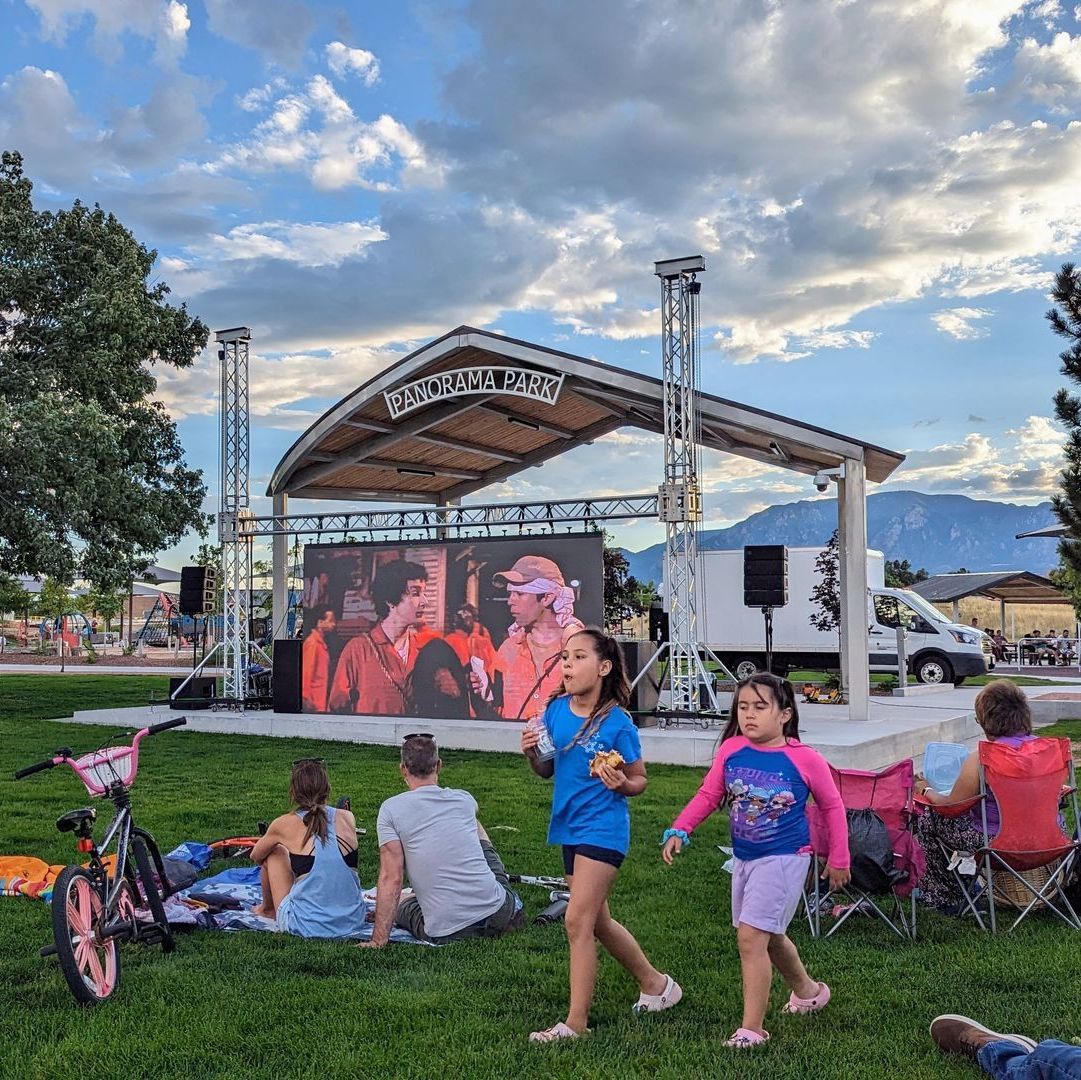 People sit on blankets on the grass in front of the Panorama Park stage for a movie night