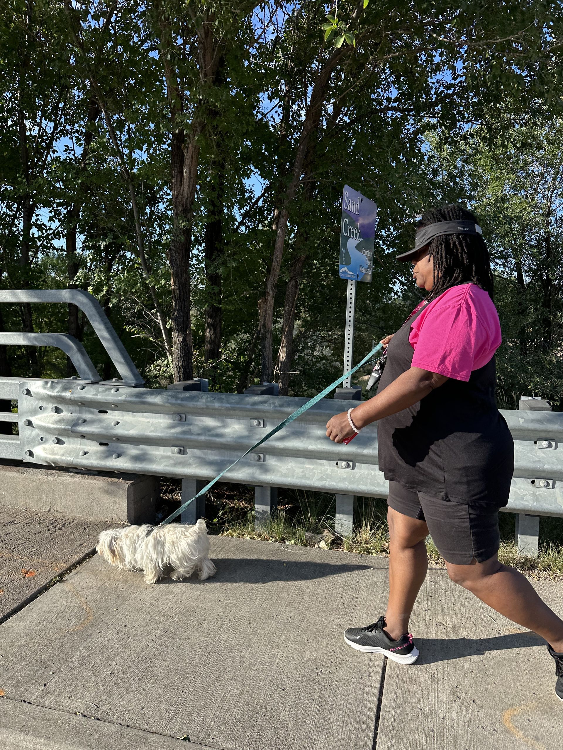 A woman is walking a small white dog on a leash.