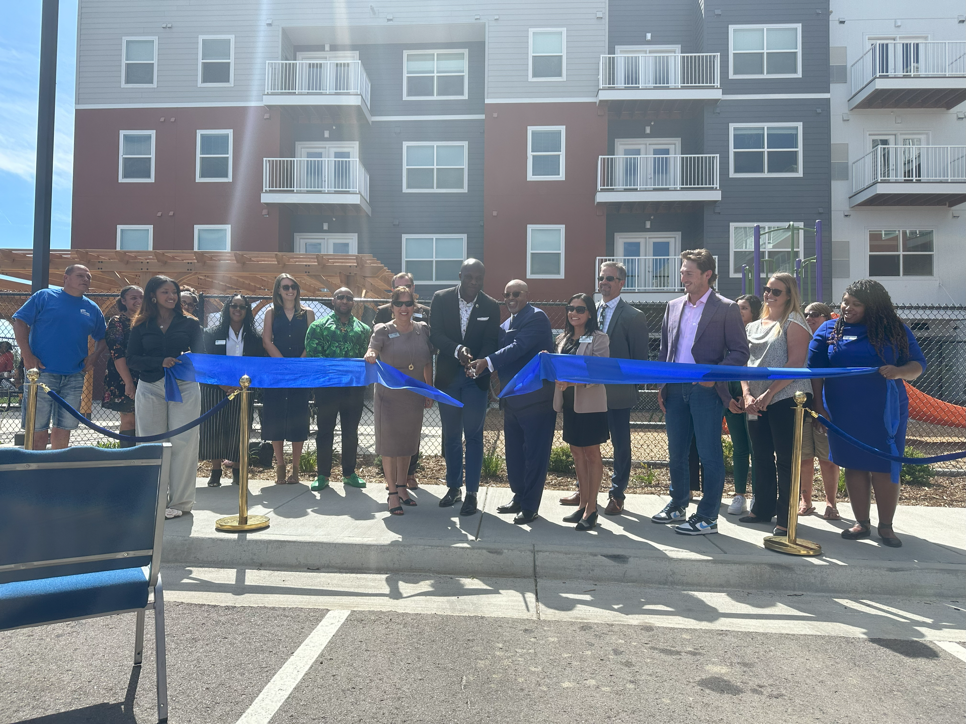 A group of people are cutting a blue ribbon in front of a building.