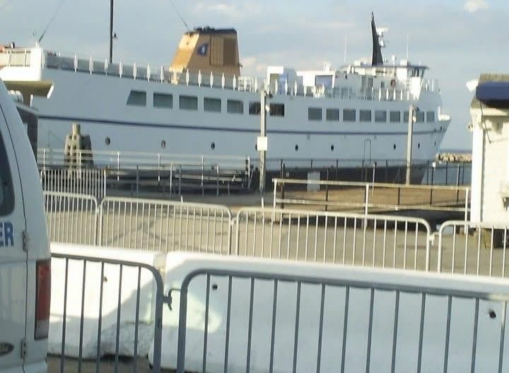 White passenger ferry docked, behind a white and silver barrier.